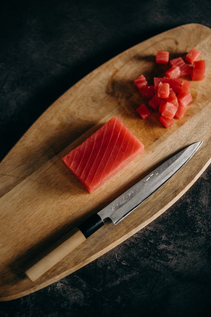 Close-up of fresh tuna cubes and knife on a wooden chopping board, perfect for Asian cuisine preparation.